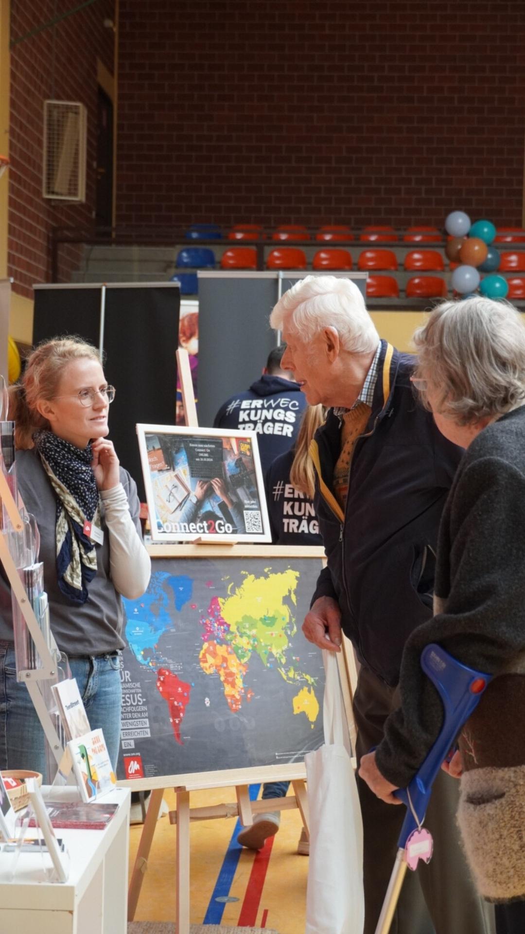 Ältere Besucher im Gespräch mit einer Missionarin am OM-Stand – JUMIKO 2024