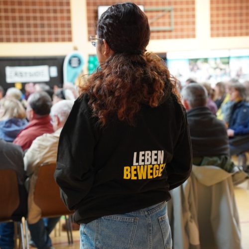 Bild vom Vormittagsprogramm, Menschenmenge sitz auf Stühlen und eine Missionarin trägt einen Pullover mit der Aufschrift "Leben Bewegen".